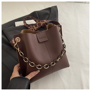 Detailed shot of dark brown pebbled leather bucket bag with golden chain and printed strap
