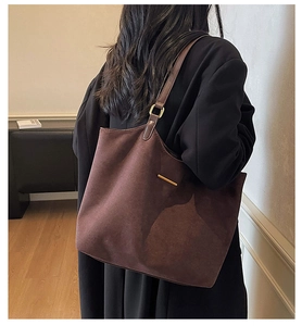 Detail of dark brown suede tote bag featuring a minimalist gold metal bar accent