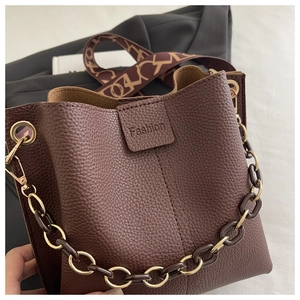 Detail of dark brown litchi grain bucket bag with chain strap and geometric strap