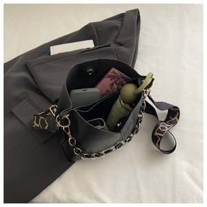 Detail of black lychee grain leather bucket bag with jacquard strap and chain accessory