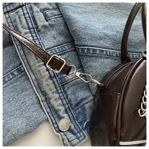 Détails macro d'un sac cabas en cuir verni marron foncé brillant sur denim bleu
