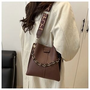 Detail of dark brown lychee leather bucket bag with decorative chain and patterned strap