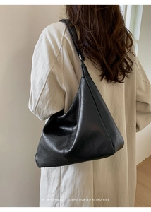Minimalist black crescent tote bag with wide strap shown on model's shoulder
