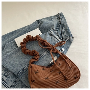 Detail of brown corduroy shoulder bag featuring black bow embroidery and scrunchie strap