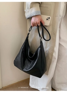 Black hobo shoulder bag with minimalist leather texture shown being carried by a model