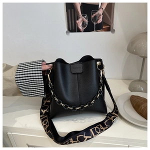 Detail of black lychee grain bucket bag with gold-tone chain and wide printed strap