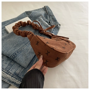 Detailed close-up of brown corduroy shoulder bag with black bow patterns and ruffled handle