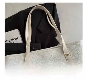 Detail of white tote bag with textured surface, gold hardware and branded logo plate