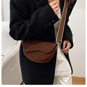 Detail of a brown suede saddle bag with a wide adjustable strap and golden metal buckle