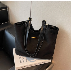Detail view of black matte tote bag featuring gold metal accents and leather shoulder straps