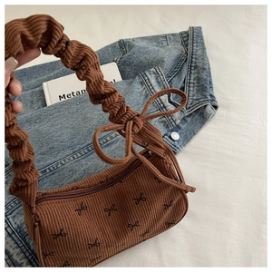 Detail of brown corduroy shoulder bag with black bow print and ruched elastic handle