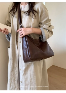 Close-up of deep brown retro leather tote bag with wide shoulder strap on a model