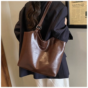 Detailed view of large dark brown leather tote bag with glossy finish on striped suit model