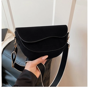 Detail of black suede saddle bag featuring wavy flap and wide contrast shoulder strap