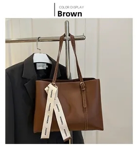 Détail d'un sac cabas en cuir mat marron foncé avec un ruban décoratif sur fond blanc