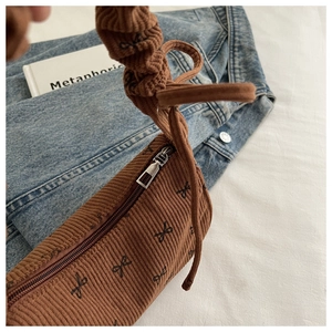 Detailed texture of brown corduroy shoulder bag featuring black bow print and zip closure