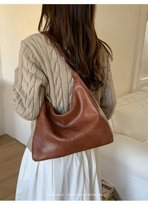 Retro brown soft leather hobo bag styled with a beige knit sweater in a minimalist setting