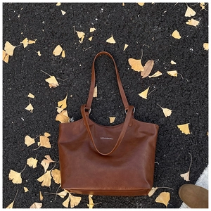 Close-up of brown textured leather tote bag on autumn leaves background with logo detail