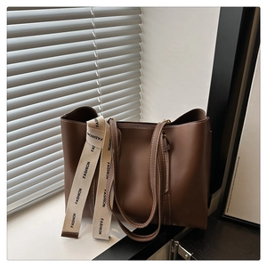 Détail d'un grand sac cabas en cuir mat marron foncé avec une bandoulière à inscription