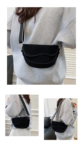 Detail of black suede saddle bag featuring a wide black and white woven shoulder strap