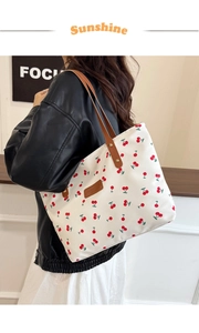 Detail of white canvas tote bag with cherry print and brown leather shoulder straps