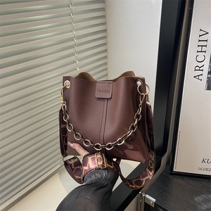 Dark brown leather bucket bag with gold chain handle and patterned strap shown in hand