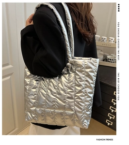 Vue latérale d'un grand sac cabas matelassé argenté porté à l'épaule sur un blazer noir