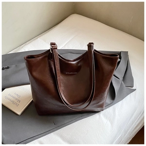 Close-up of deep brown leather tote bag with brand logo on white bedding