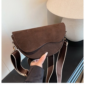 Detail of dark brown suede saddle bag featuring wide woven strap and fashion branding