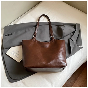 Detail of dark brown leather tote bag with glossy oily finish on a grey suit jacket
