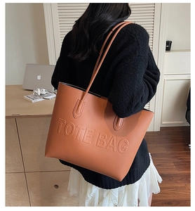 Brown leather tote bag with embossed text shown on a shoulder in a modern office setting