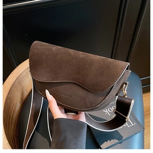 Detail of coffee brown saddle bag featuring suede flap and wide woven shoulder strap