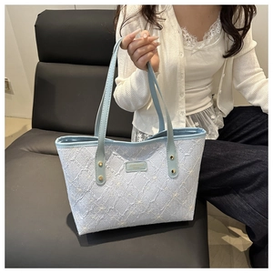 Close-up of light blue tote bag with 3D bow embroidery and metallic brand plate