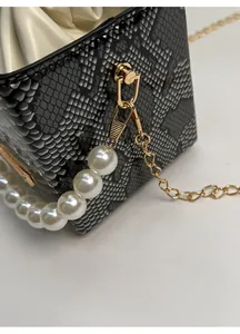 Detail of gold metal clip connecting chain strap to snakeskin pattern bucket bag