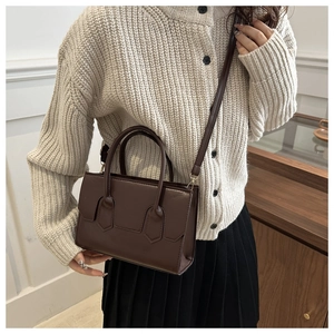 Detail of a dark brown PU leather handbag styled with a cream sweater and black skirt