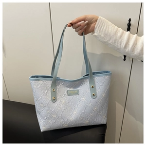 Detail of light blue textured tote bag featuring white bow embroidery and brand plaque