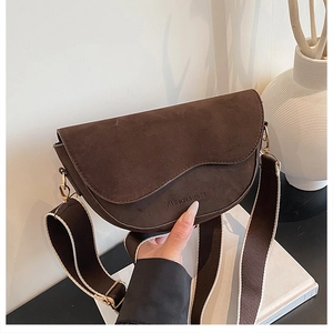 Detail of dark brown matte leather saddle bag featuring gold hardware and wide woven strap