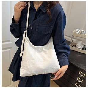 Détail d'un grand sac bandoulière blanc en toile porté sur une robe en jean bleu