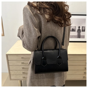 Model wearing a black leather crossbody bag with top handle and decorative stitching