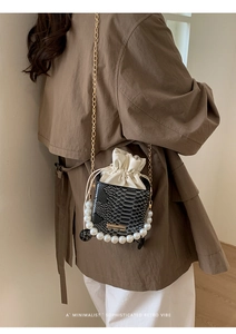 Detail of snake pattern texture and pearl handle on a luxury crossbody bucket bag