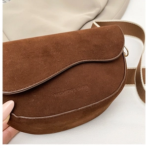 Détail du sac selle en daim marron avec bandoulière tissée et logo embossé