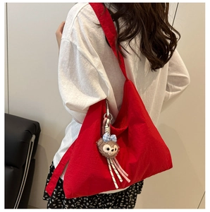 Détail du sac bandoulière rouge en toile avec un pendentif ours en peluche et nœud écossais