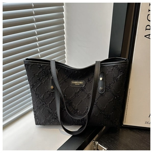 Close-up of black sequined tweed tote bag with a golden metal logo plate on window sill