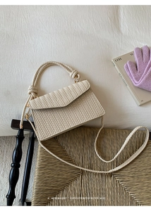 Detail of beige herringbone woven handbag with unique rope knot handle on a textured chair