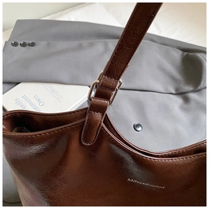 Detail of a dark brown large tote bag with shiny finish and silver metal buckle adjustment
