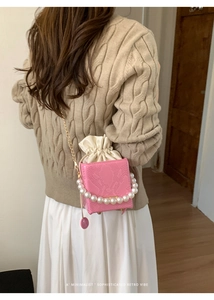 Pink croc-embossed bucket bag featuring a pearl top handle and elegant drawstring closure
