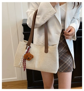 Detail of beige canvas tote with brown leather strap and cute bear plush charm decoration