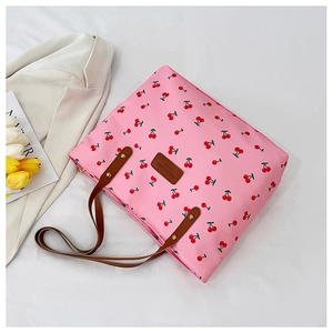Detail shot of a pink canvas tote bag with cherry print and brown leather handles