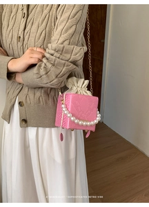 Detail of pink croc-effect box bag featuring pearl handle and gold chain strap
