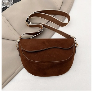 Close-up of brown suede saddle bag with wave-edge flap and wide woven strap